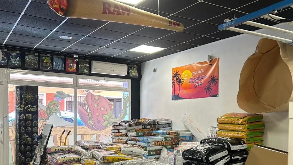 Sacos de sustrato apilados junto a la entrada del local, con el escaparate al fondo